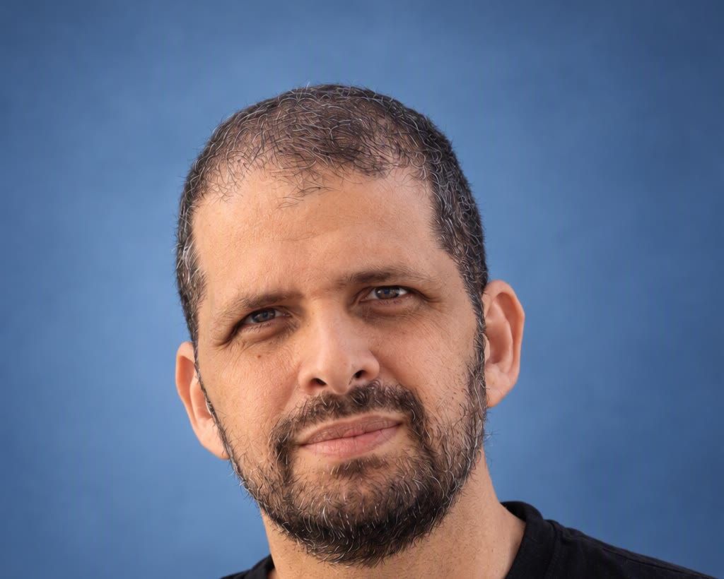 AI headshot of a man with a light, real smile against a blue studio backdrop, made by CMeIn from his own photos