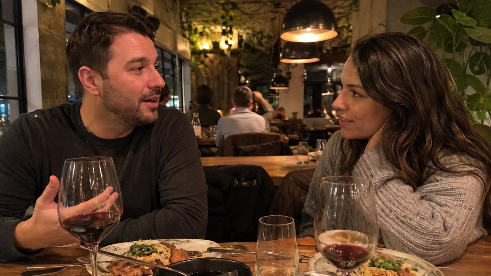 Two people deep in conversation across a small table, one mid-story, the other listening intently