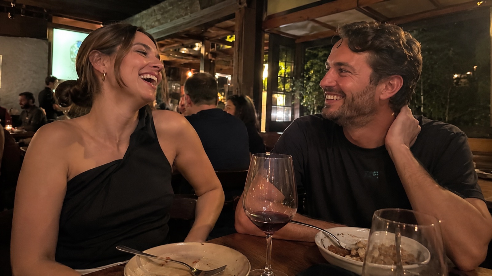 A couple laughing together across a small restaurant table in warm evening light