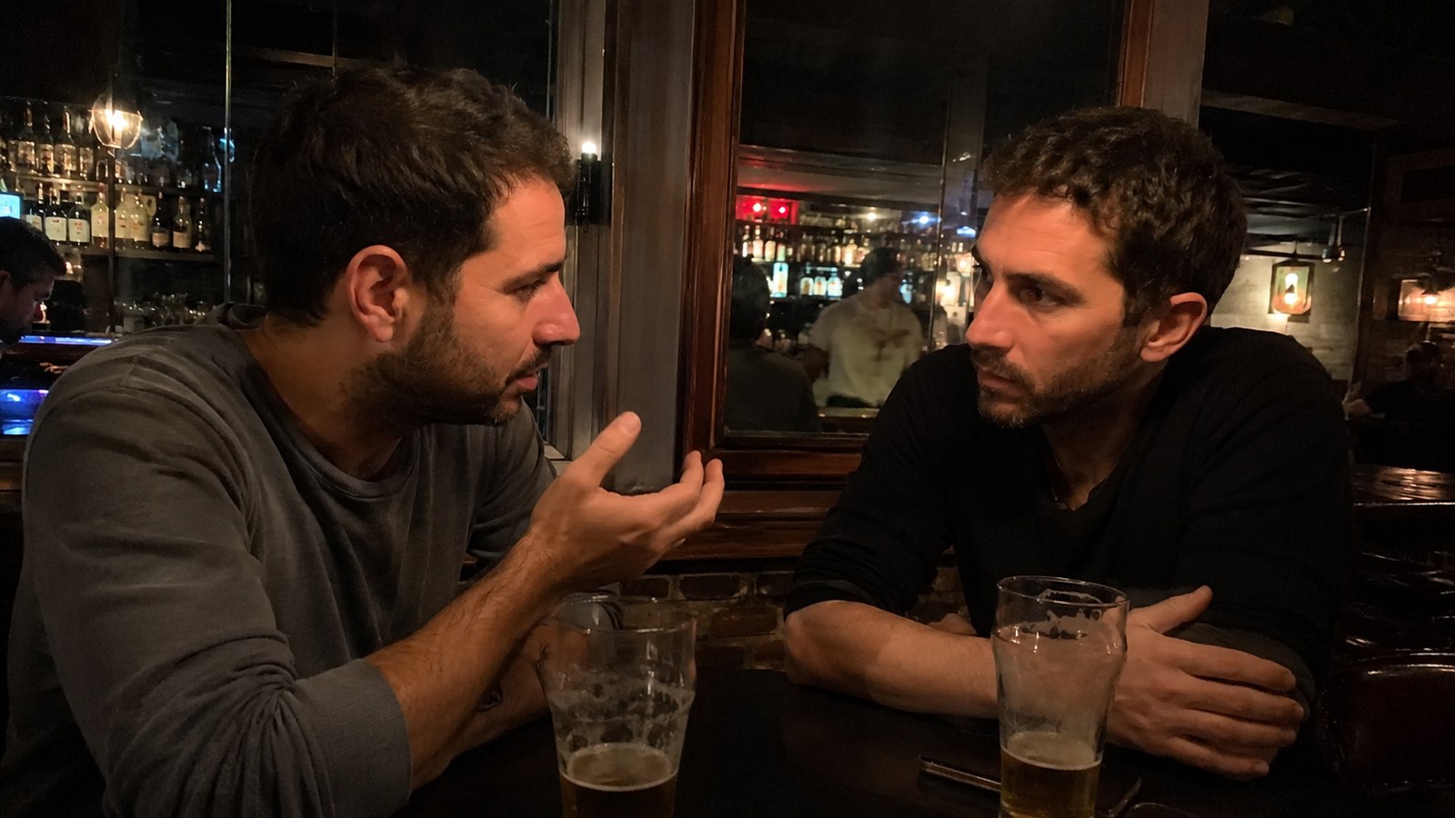 Two friends in a serious talk over beers at a bar table