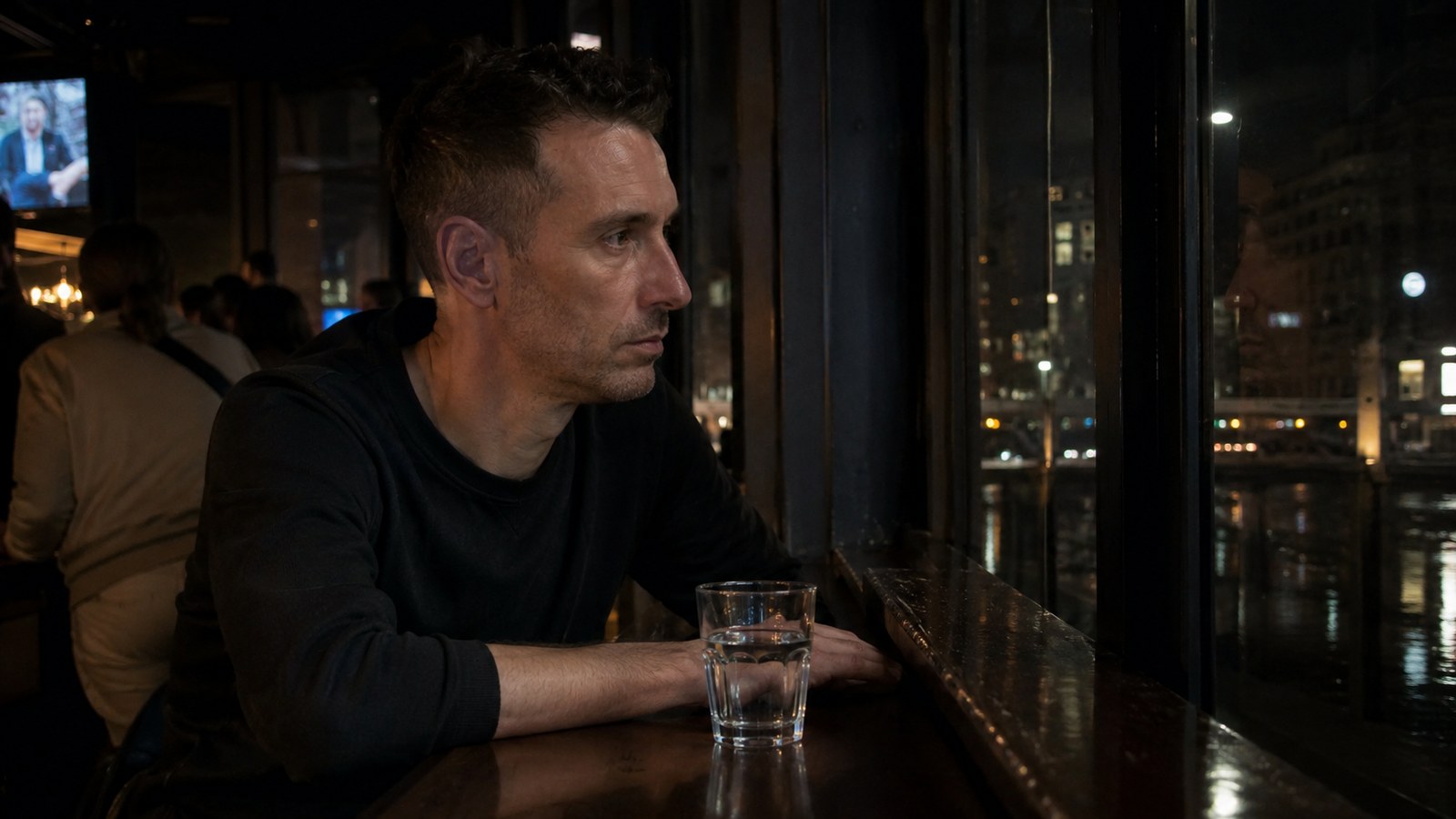 A man alone with his thoughts at a bar window, city lights outside