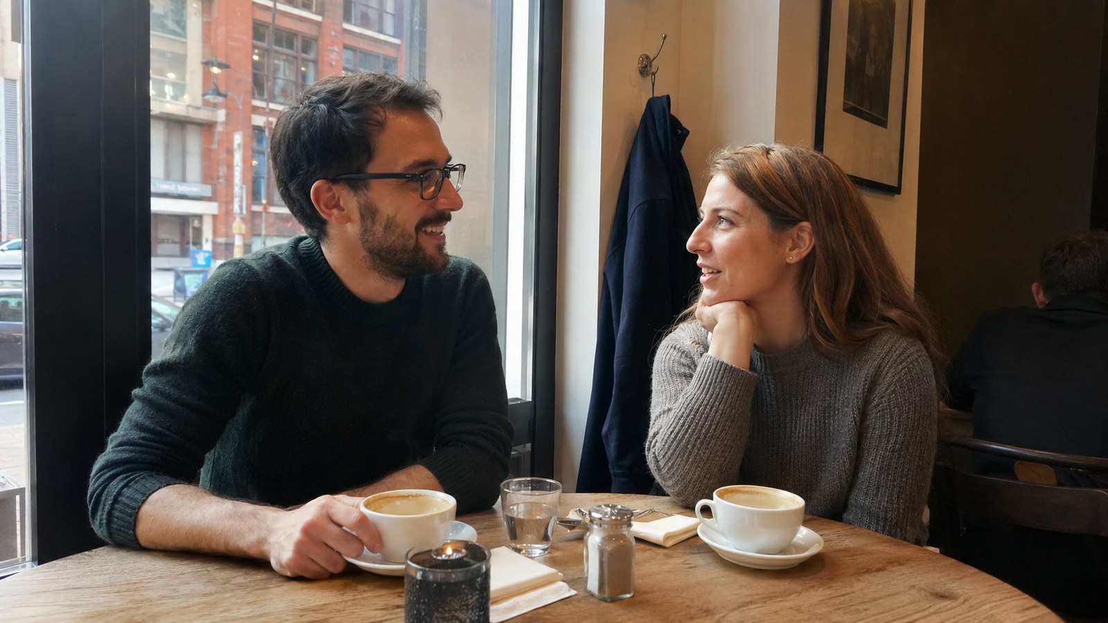 A couple talking over coffee at a window table, relaxed and open