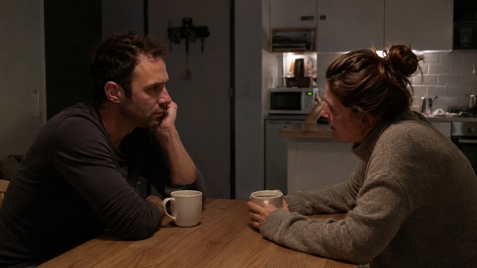 A couple in a quiet, serious conversation at a kitchen table