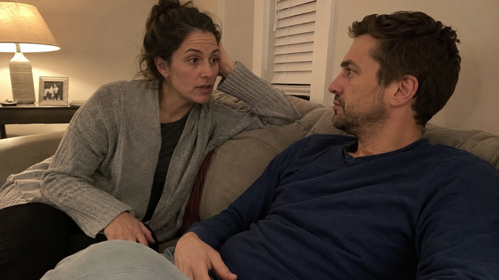 A couple on a couch mid-conversation, lamplight, honest expressions