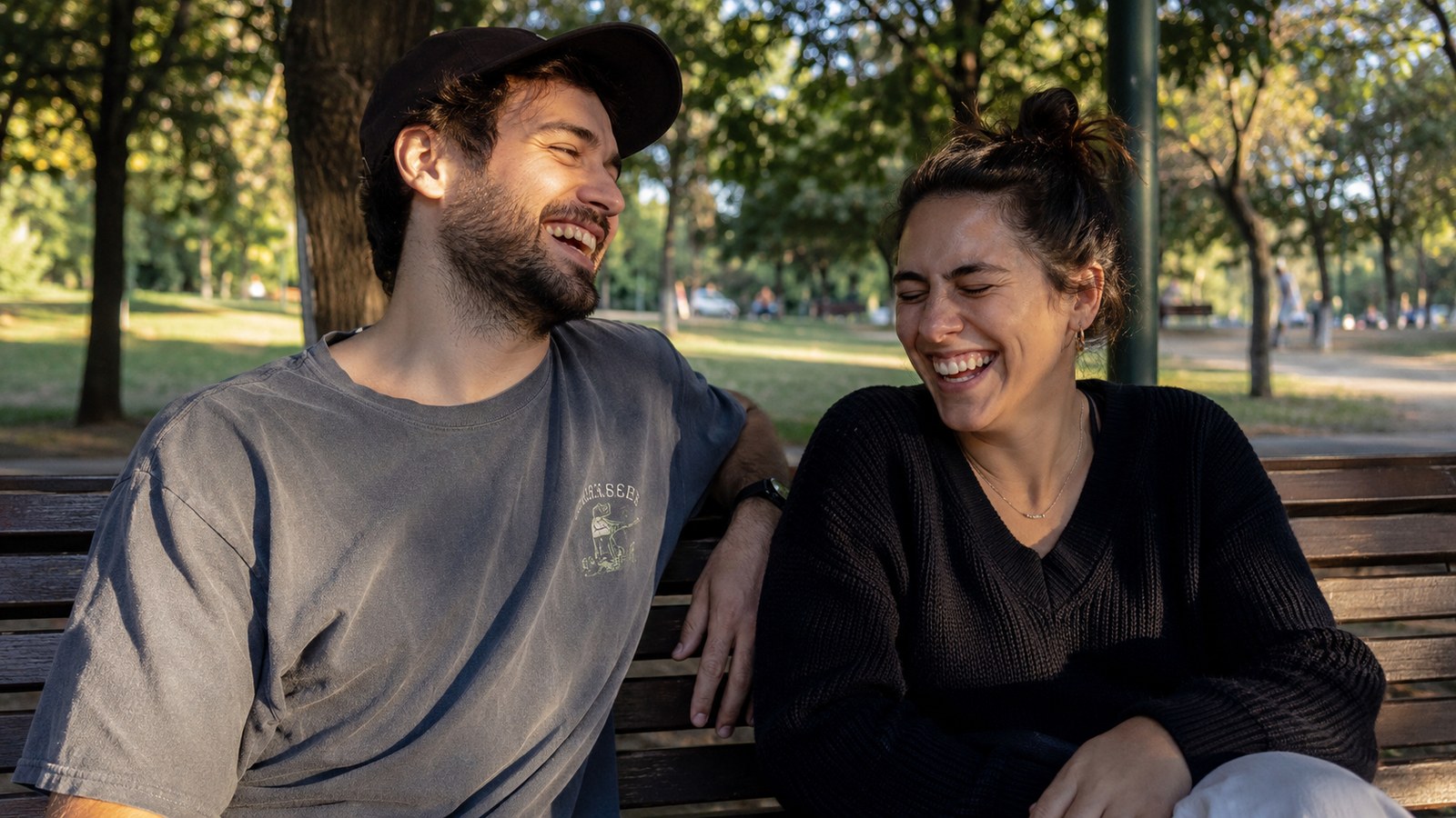 Two friends laughing on a park bench, easy and unposed