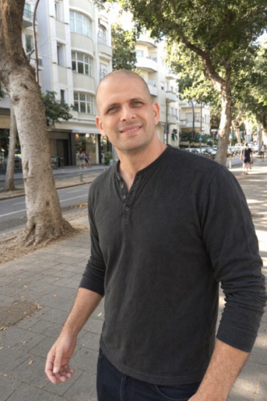 Man walking down a sunny tree-lined boulevard with a slight smile, phone nowhere in sight