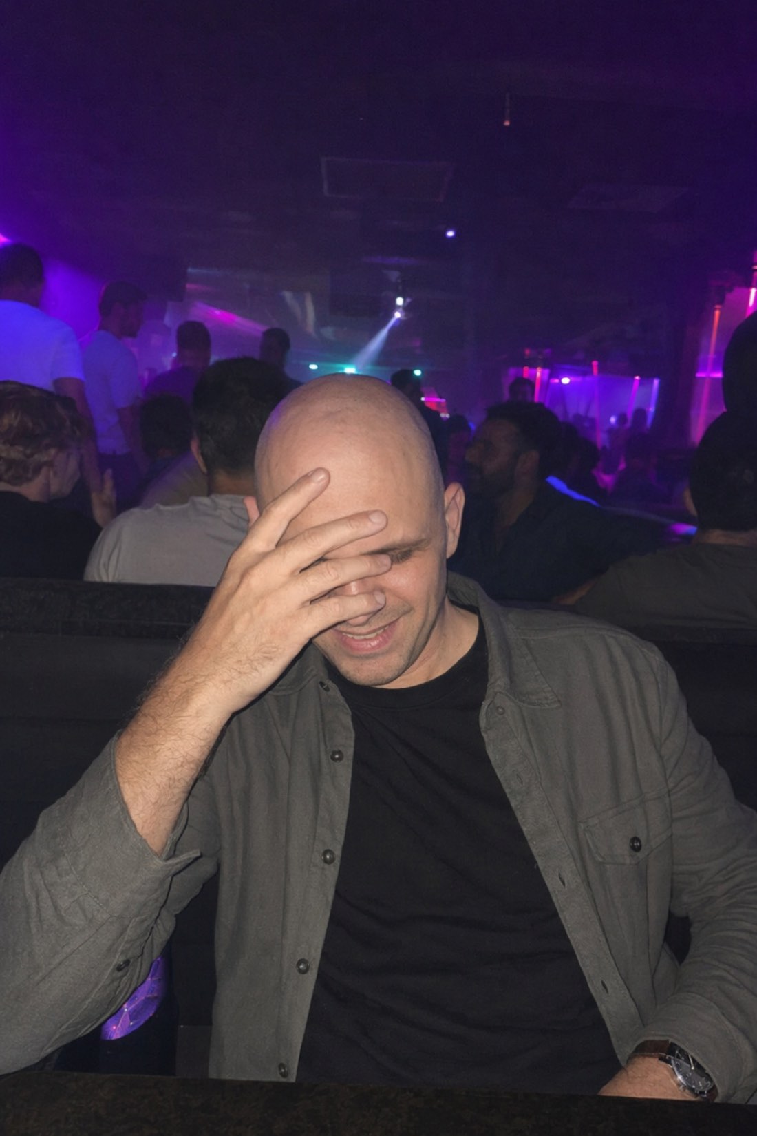The avoidant reflex in one frame: warm moment, hand up anyway. Man laughing behind his hand at a nightclub