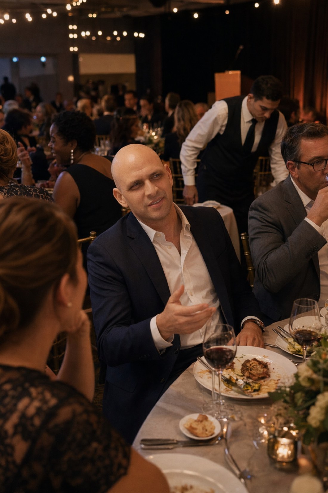 Man in a navy suit talking at a formal dinner, a professional photo made without a photographer