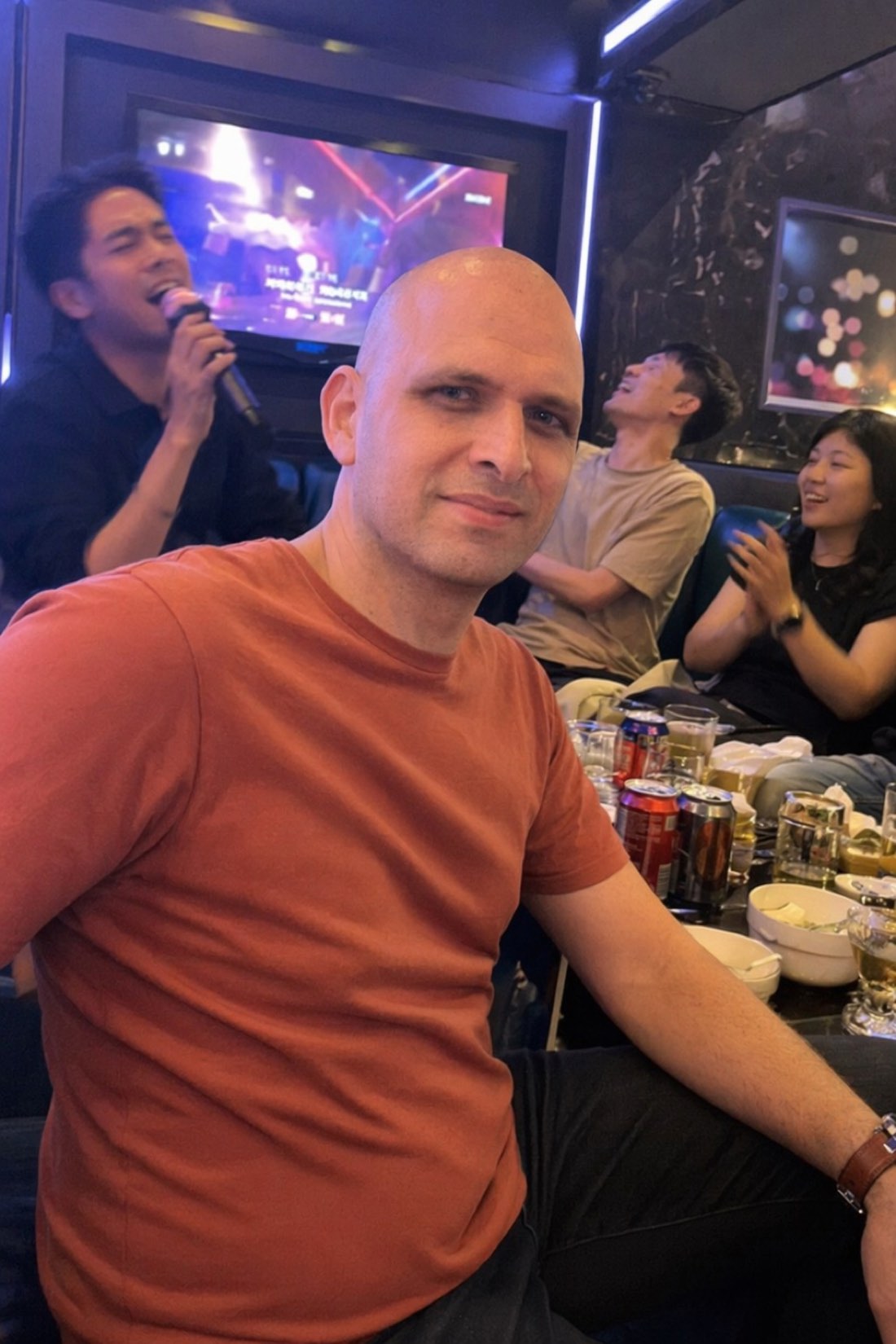 Present at the party, busy monitoring it. Anxious attachment is never quite off duty. Man sitting slightly apart and tense while friends party at a karaoke room