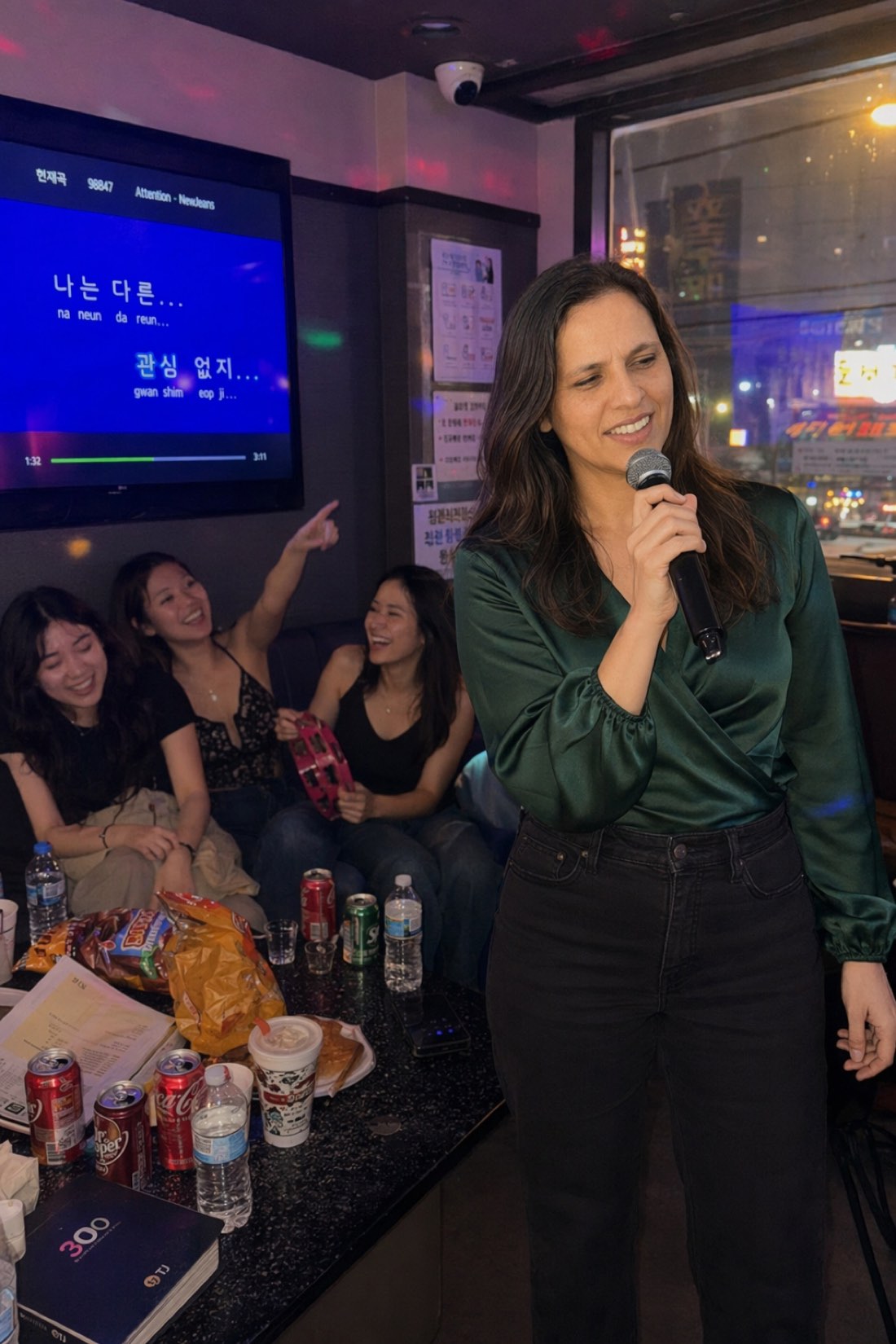 Woman singing karaoke with a mic while friends cheer with a tambourine, the kind of photo that starts conversations by itself