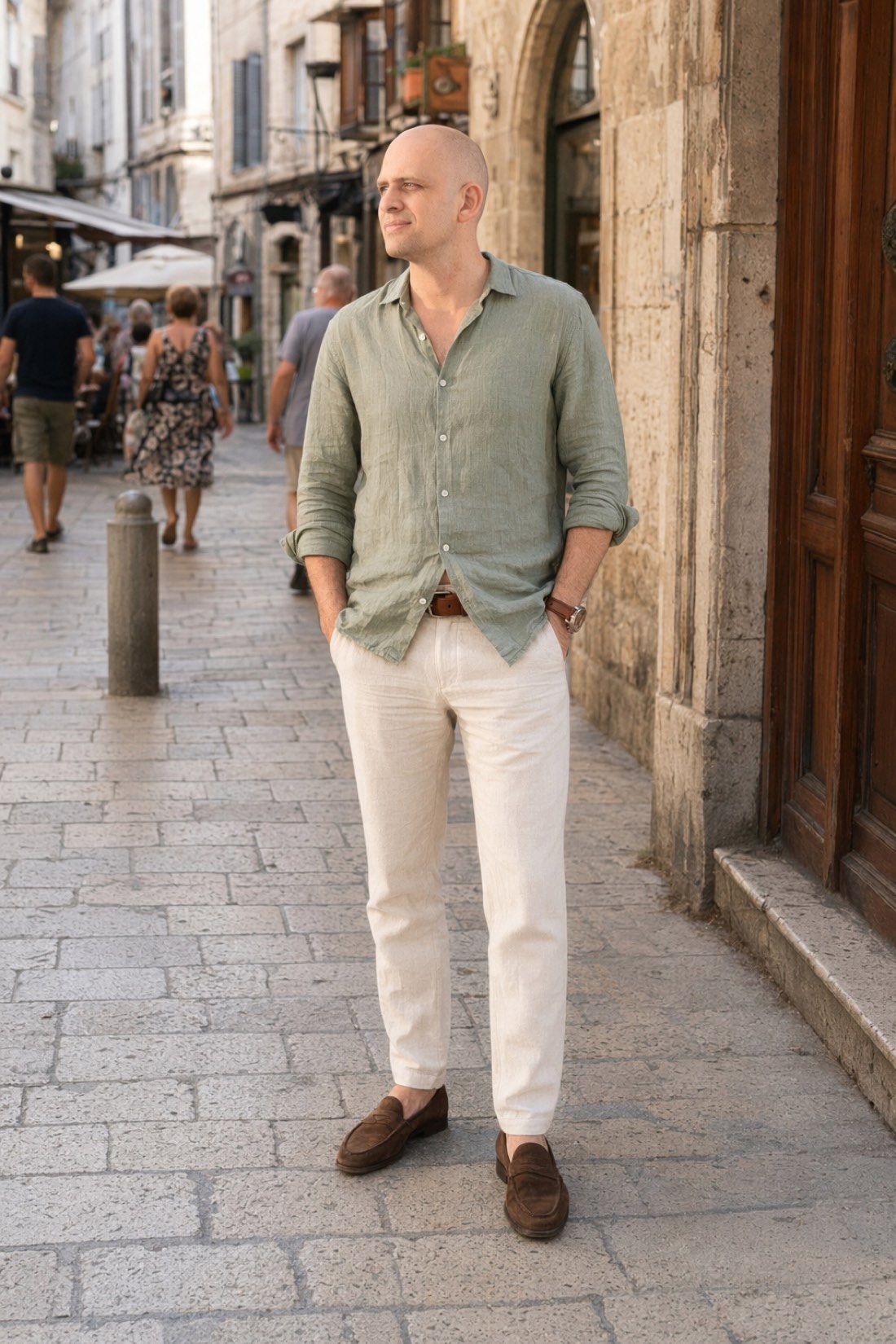 Man in a sage linen shirt, cream trousers and suede loafers on an old town street, the whole playbook in one outfit
