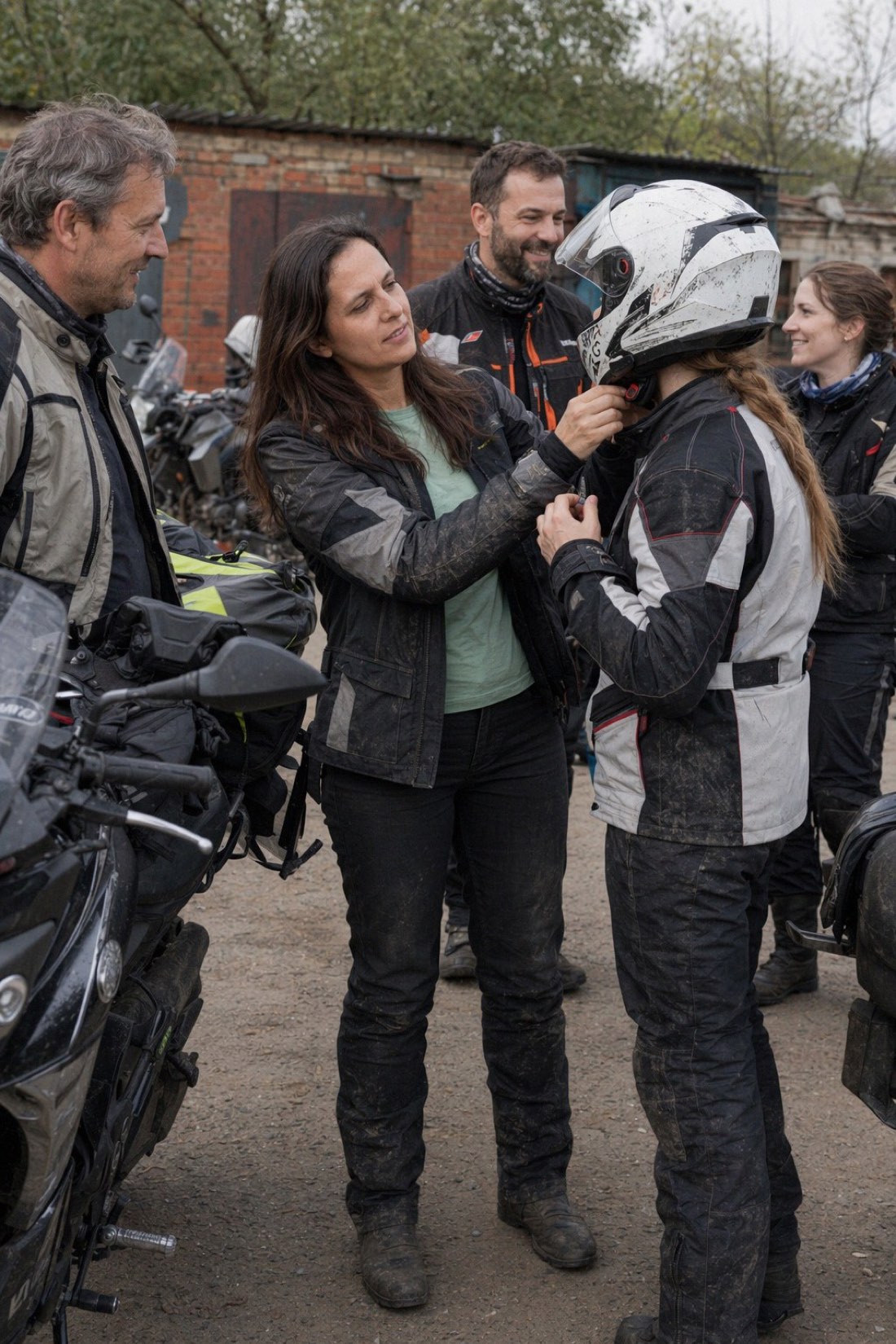 Woman helping a friend fasten a motorcycle helmet before a group ride, character shown instead of claimed
