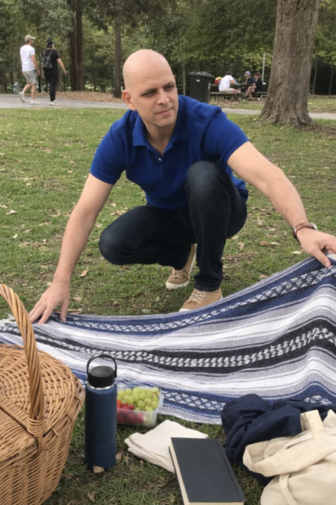 Man crouching over a picnic blanket in a park