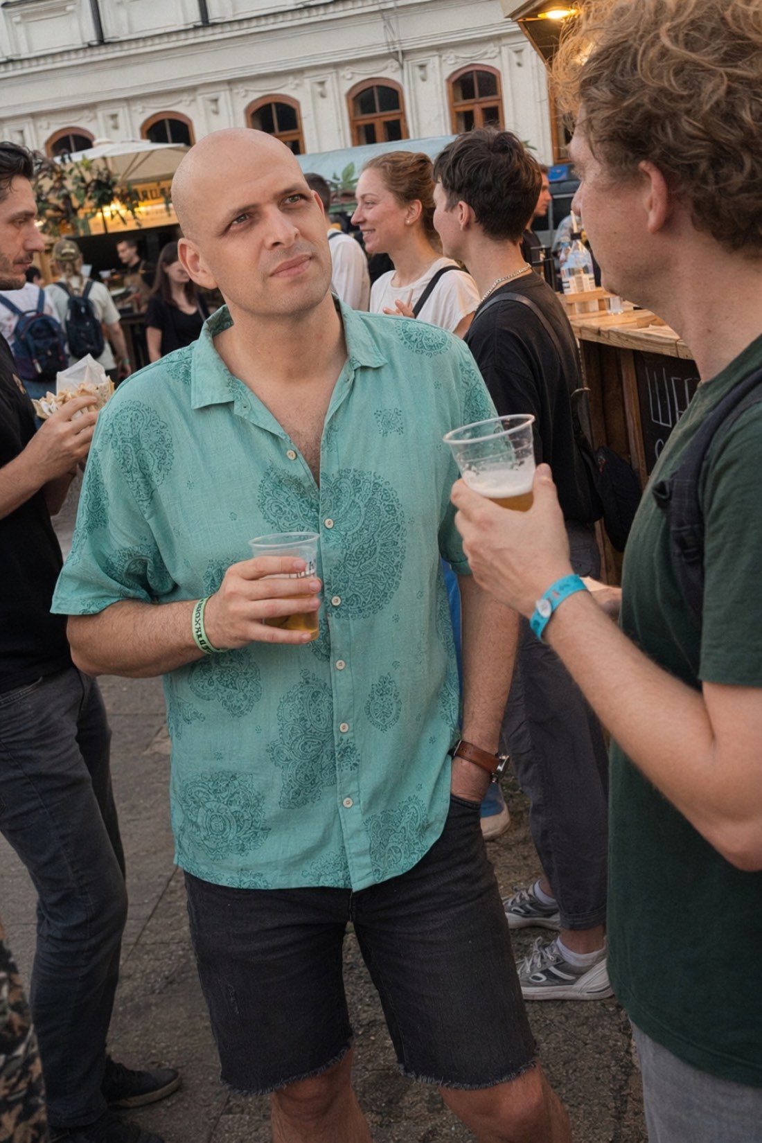 Man in a teal shirt with a drink at a street festival