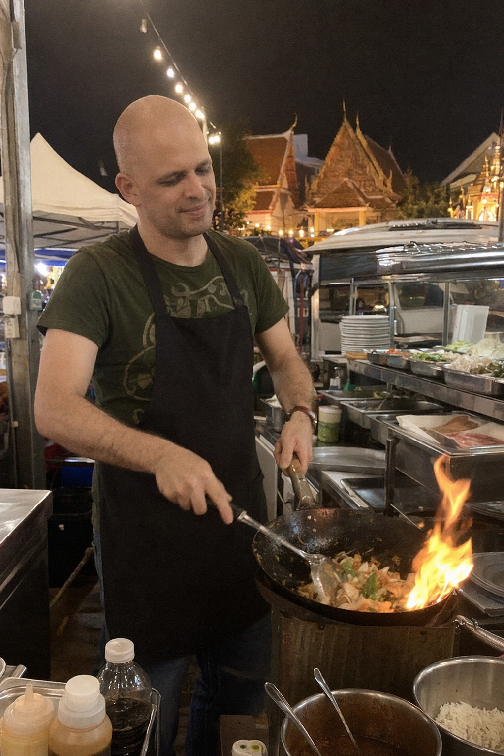 A wok catching flame on a home stove, phone propped against the tiles filming