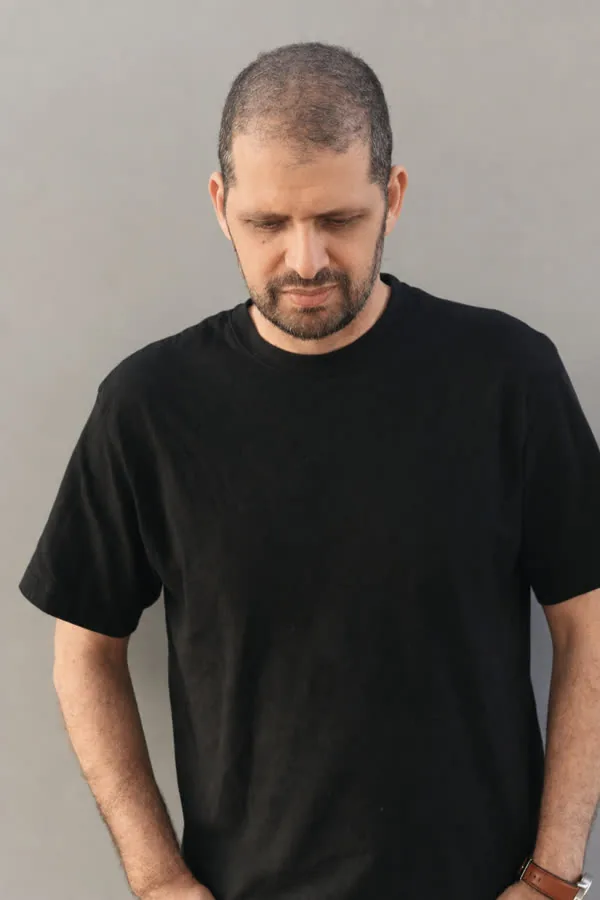Reference photo: a man with short greying hair and a beard, head lowered, plain wall behind him