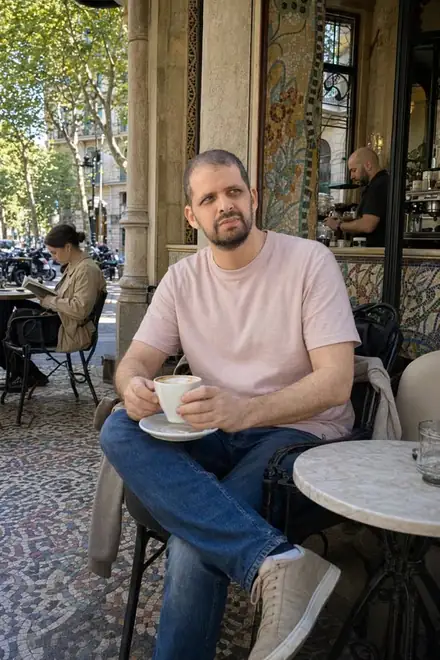 Generated photo: the same man sitting outside a cafe with a coffee
